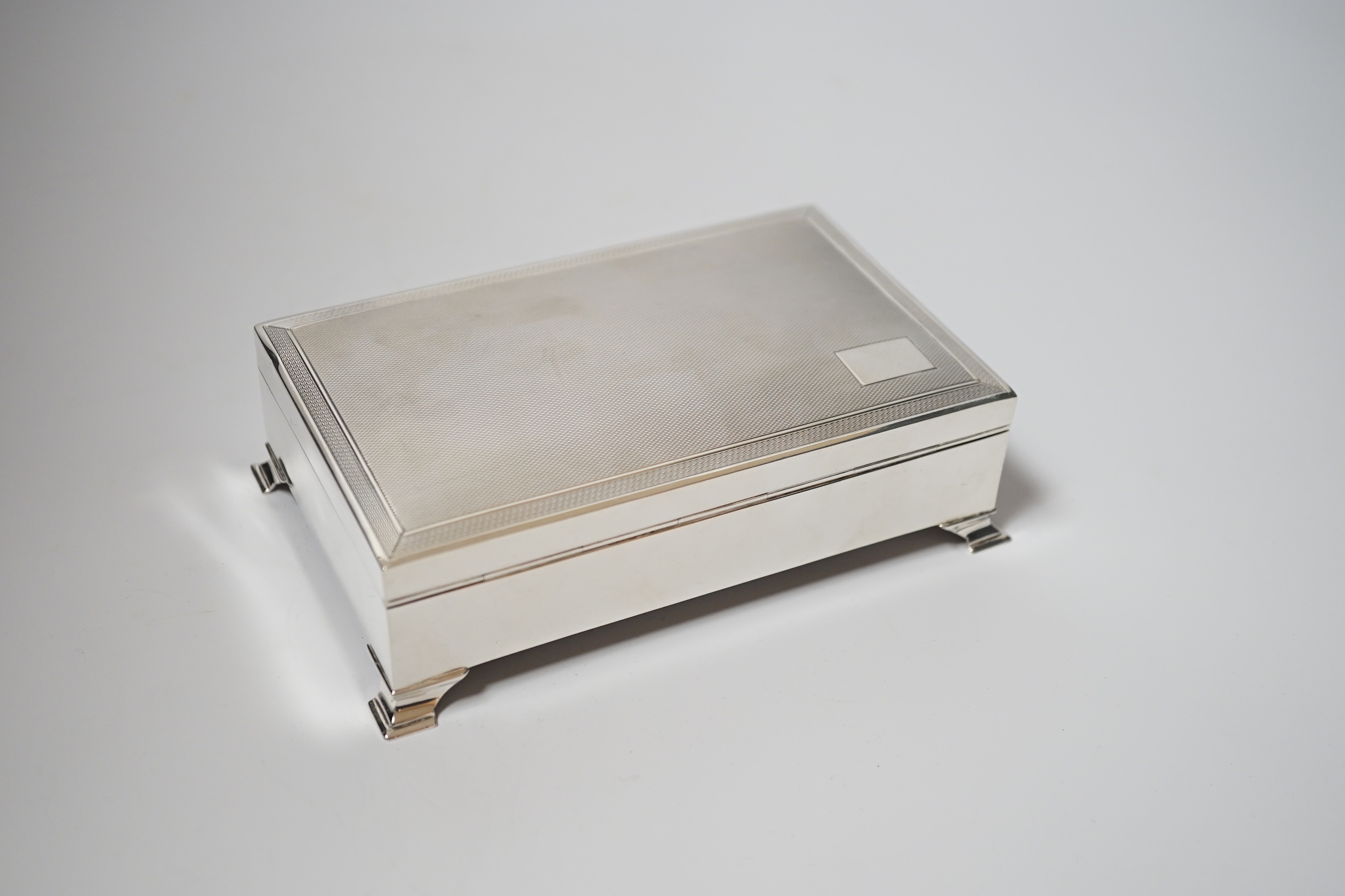 An Elizabeth II engine turned silver mounted rectangular cigarette box, Birmingham, 1961, 15.4cm, on bracket feet.